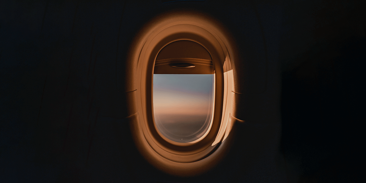 A colorful sky is visible outside the partially opened window in an airplane.